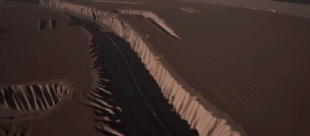 A dark brown landscape with a deep river channel running between a tall pale ribbed cliff wall and broken ground, with a thin white line along the channel floor.