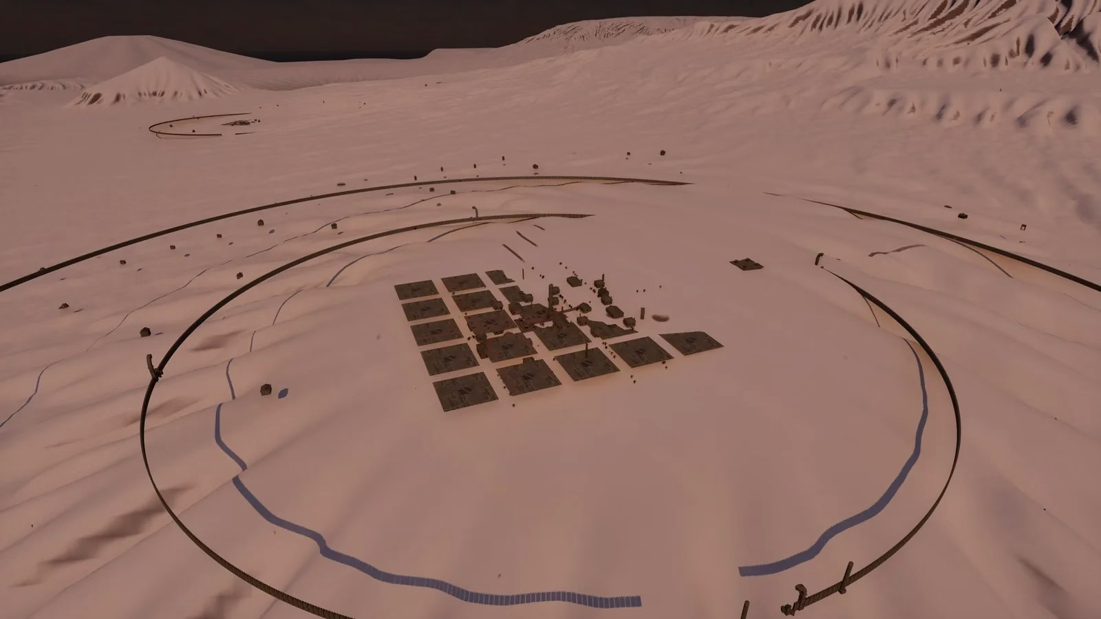 A small grid of dark flat slabs with a few tiny buildings, sitting inside two thin rings of wall on wide, empty white ground, with bare white hills and mountains behind.
