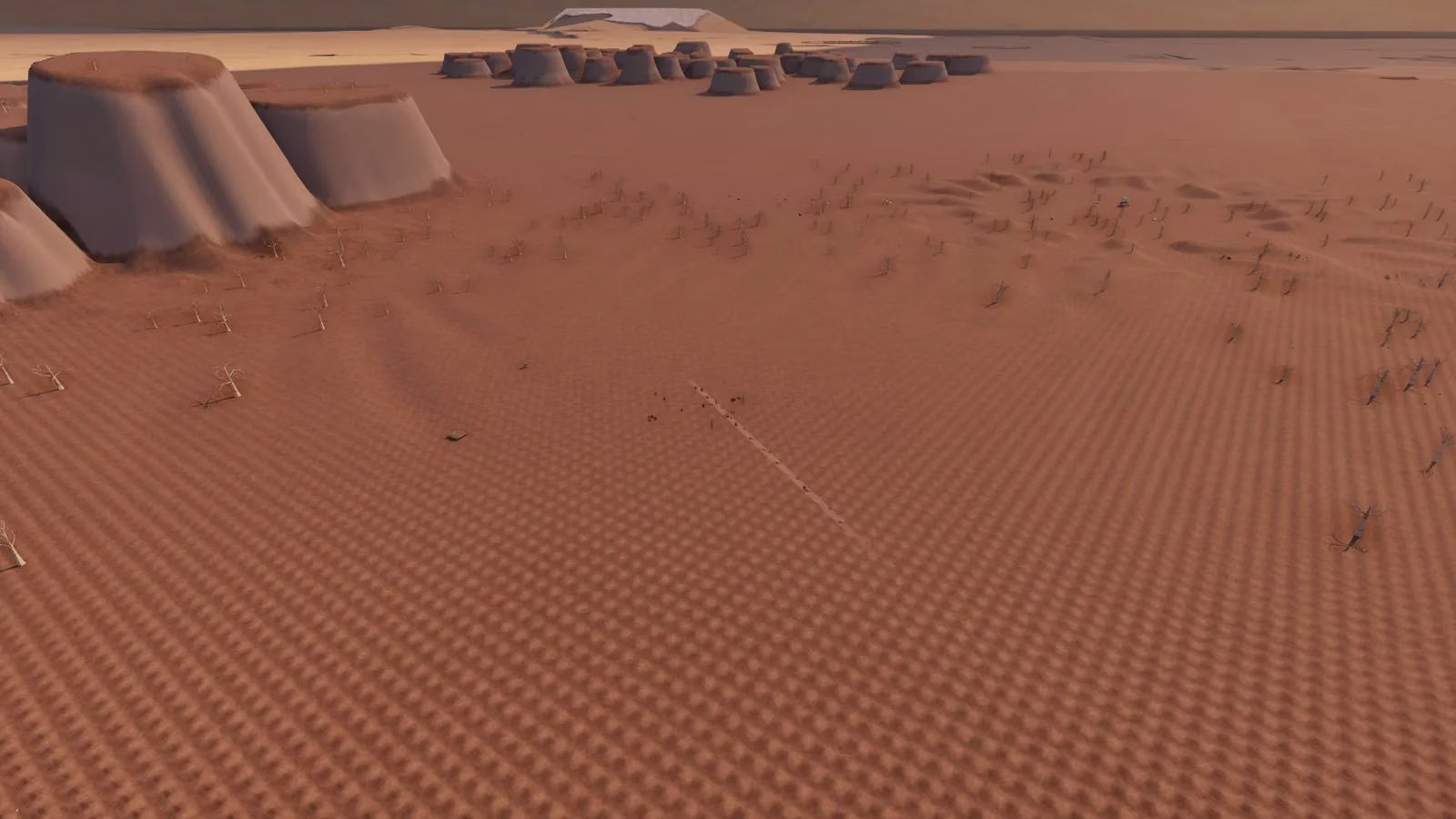 A wide plain of rippled orange sand dotted with bare dead trees, two flat-topped mesas at the left, and a cluster of low drum shapes far off near the horizon.
