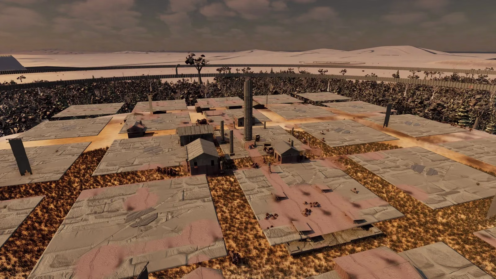 A raised view of a town of flat grey paving slabs on dry orange grass and sandy paths, with a few small wooden huts and a tall stone pillar in the middle, a dark forest and a wooden wall around it, and pale dunes beyond.