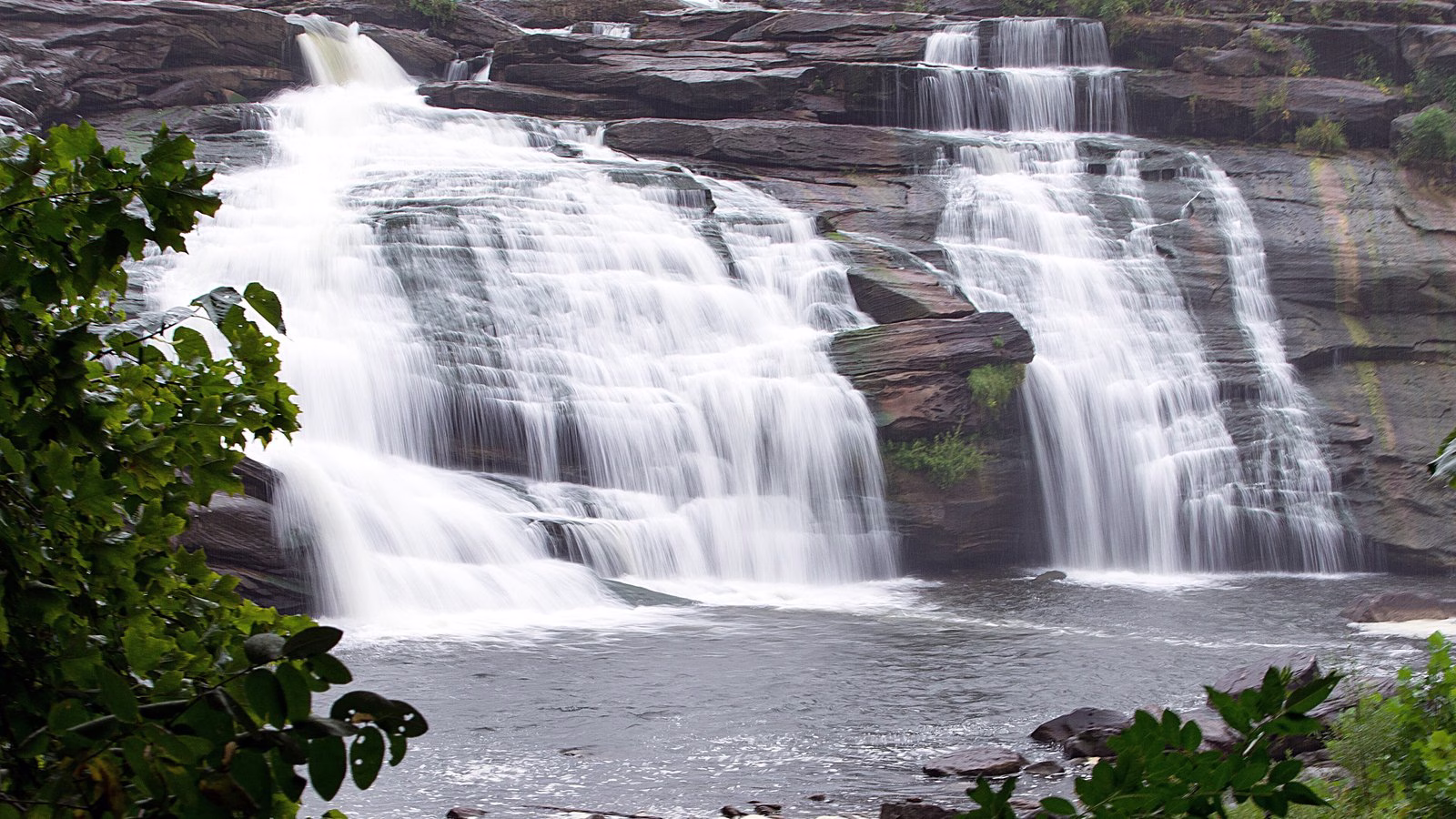 Wide white cascades pouring over layered dark rock.