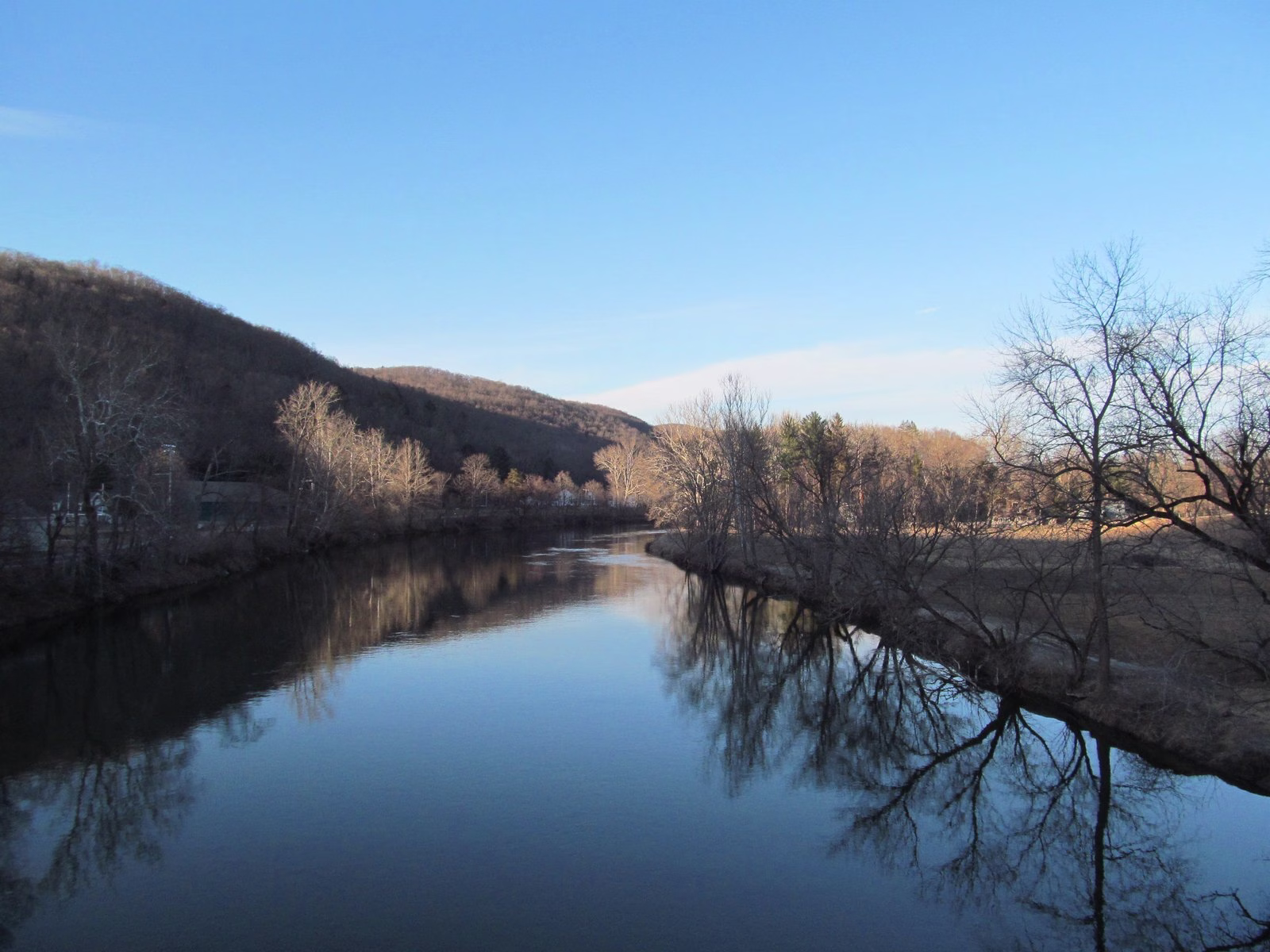 A still blue river mirroring bare trees and hills.