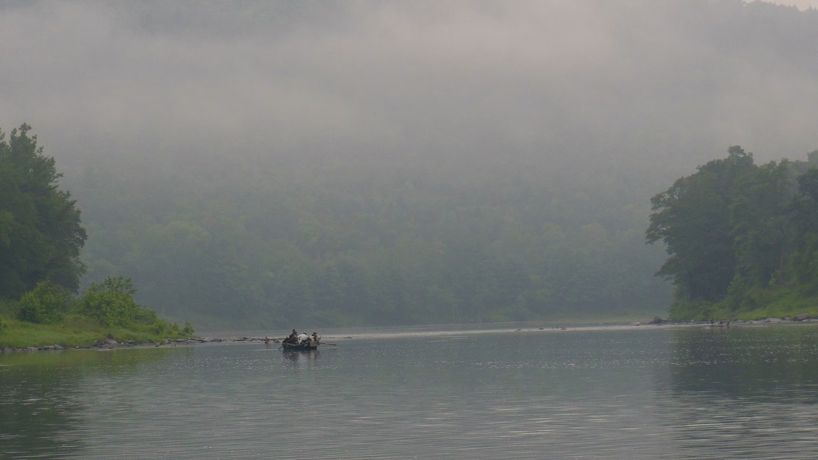 A small boat on calm water under fog-wrapped wooded hills.