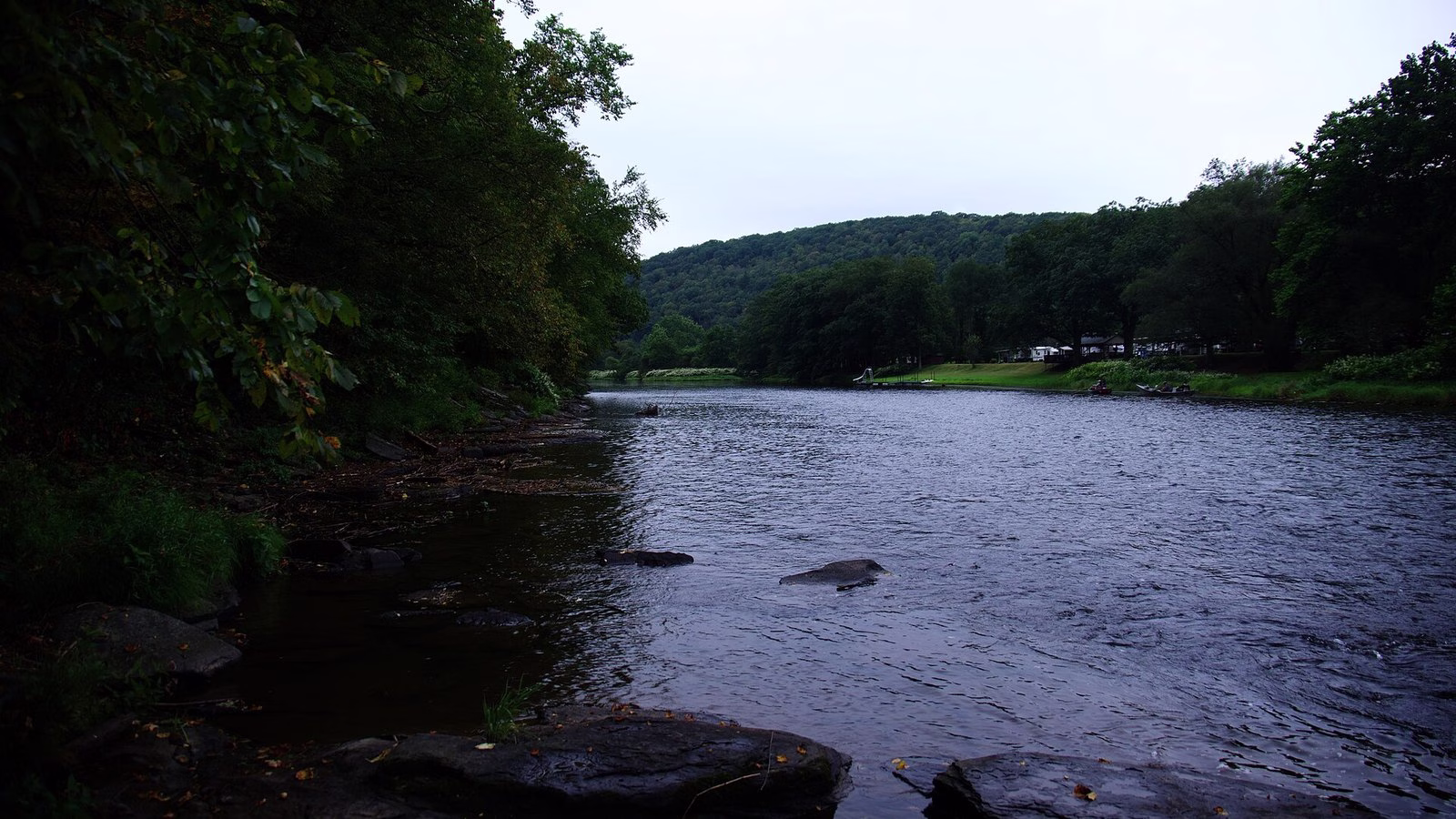 A broad riffled river curving between forested hills.